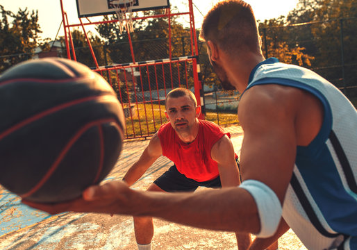 Two friends playing basketball on court outdoors at sunset.	