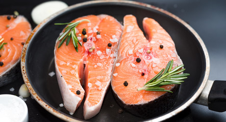 raw salmon steak on a dark stone background with onions, rosemary, spices, concept diet, unsaturated fats, omega 3