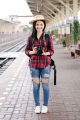 Young beautiful female travel photographer enjoys taking photo during her trip at railway station. Asian woman travel with camera having fun making pictures while waiting for train.