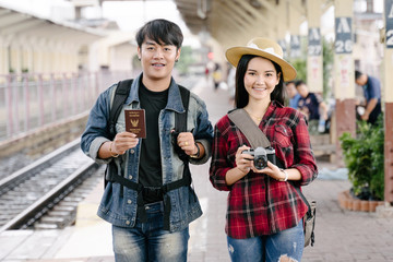 Fototapeta na wymiar Couple of travel photographer enjoys taking photo during their trip at railway station. Asian travelers with camera having fun making pictures while waiting for train.