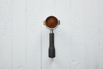 Top view of portafilter with coffee on white wooden surface