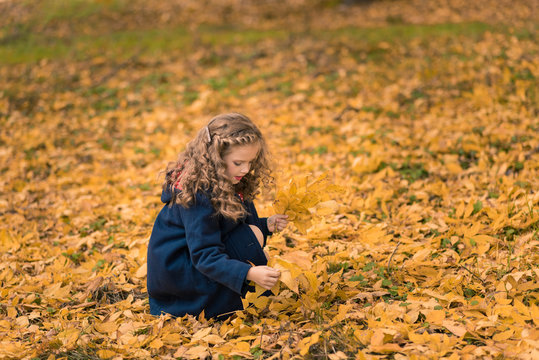 Pretty girl with long curly hair in the autumn park on the background of yellow leaves dancing. Excited cheerful girl drop up leaves, joyful with beautiful autumn colors