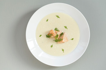 Creamy soup with salmon, potatoes, onions, carrots and dill in a bowl. A bowl of creamy soup with salmon on a grey background, top view.