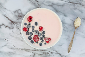 Yogurt Smoothie Bowl Topped with Frozen Berries. Smoothie bowl with berries raspberries, blueberries and with coconut flakes on a light marble table. Top view. Healthy breakfast. Vegetarian food