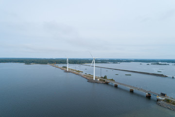 Three spinning wind turbines near a river in a countryside area. A car passes on the nearby road. 