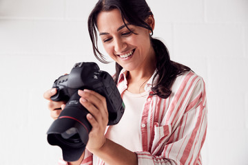 Female Photographer With Camera On Photo Shoot Against White Studio Backdrop