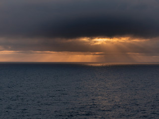 Fototapeta na wymiar Dark and moody sky over the ocean, Sun shines through the clouds, Orange and dark color.