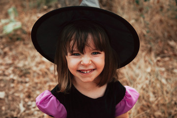 Smiling girl disguised as a witch in the woods during Halloween