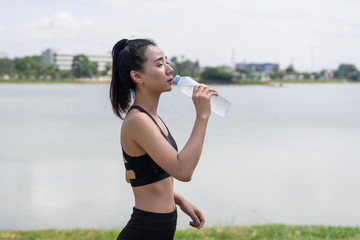 Young woman runner wear white sporty vest, white cap, black short pant do stretching before and after running exercise. Woman runner stretching legs before run during sunny morning on city road.