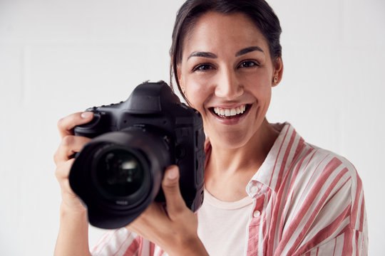 Portrait Of Smiling Female Photographer With Camera Against White Studio Wall