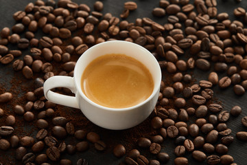 White ceramic cup with espresso on surface with scattered coffee beans