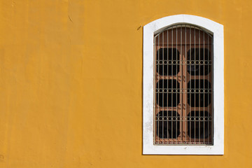 Fototapeta na wymiar Large wooden window with railings and white border on the yellow wall of an old house