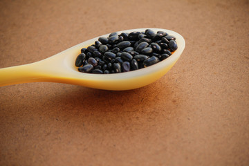 Portion of raw black bean on a yellow silicone spoon with wood background