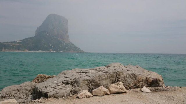 Stunning view of Penyal d'Ifac and calm mediterranean sea with rocks on foreground