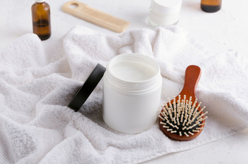 Fototapeta na wymiar Plastic jar of balm for hair, wooden brush and com, bottles of oil on the white towel