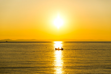 Fishing boat at sea, against setting sun.