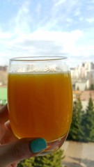 A glass with yellow orange juice against the blue sky. A glass of orange juice in his hand