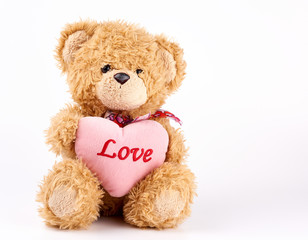 beige teddy bear holds a pink heart, white background