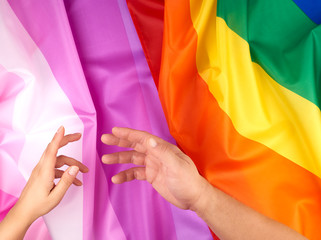 female and male hand outstretched against the background of flags of LGBT communities