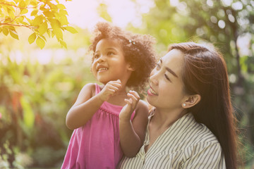 Cute young daughter with her Asian parent or Child care staff relaxing and enjoying in nature on outdoor. Mother with her 5 years old kids playing together in a park. Mother day. family, life concept - Powered by Adobe