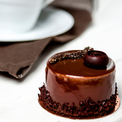 A delicious chocolate cake with chocolate pieces lies on a wooden stand next to a white cup, which stands on a white table