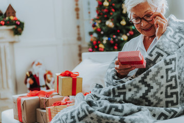 Senior woman in glasses is sitting with Christmas presents