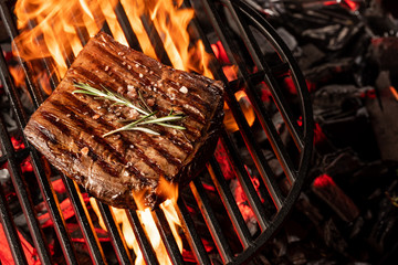 Cooking beef meat steak on hot grill barbecue with fire flams and smoke on black background.