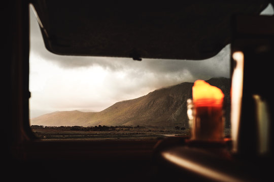 Brennende Kerze vor ge&ouml;ffnetem Fesnster in einem Camper Van / Wohnwagen mit einem Bergmassiv in Hintergrund