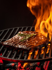 Hot juicy meat steak on hot grill barbecue with fire flams and smoke on black background.