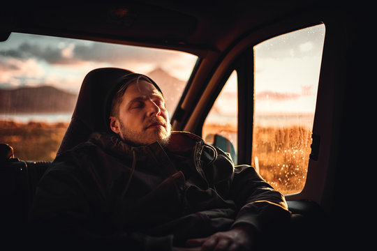 Mann schl&auml;ft in einem Camper Van bei sonnenuntergang, im Hintergrund Berge und das Meer.