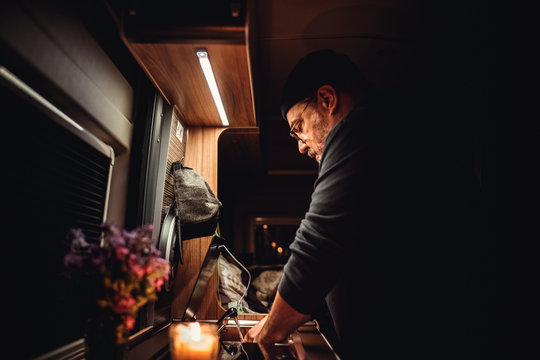 Mann mit Bart Brille und M&uuml;tze w&auml;scht abends nach dem kochen im Camper das Geschirr ab auf der K&uuml;che stehen noch Blumen und Kerze