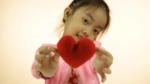 Asian little girl showing red heart pillow