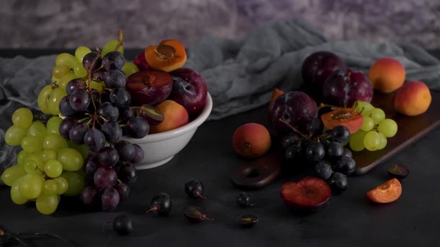 Fruits Still life with fruit on white ceramic bowl. Concrete wall. Dramatic light. Grapes, apricots and plums.