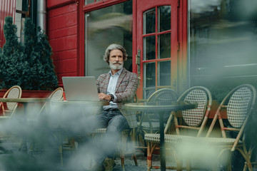 Bearded senior man using laptop at outdoor cafe
