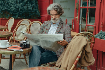 Elegant senior man reading daily news at outdoor cafe