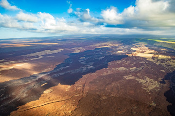 Fototapeta na wymiar Aerial view of lava fields over Kaimu'Uala go off into the horizon with flat clouds and bright green on the right