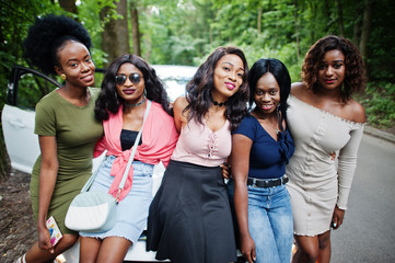 Group of five happy african american girls sitting on a car hood.