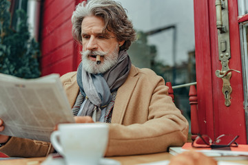 Elegant senior man with cigar reading newspaper
