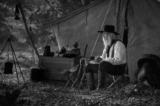 Vintage image, of a man dressed in a cowboy outfit, sitting and relaxing at his camp
