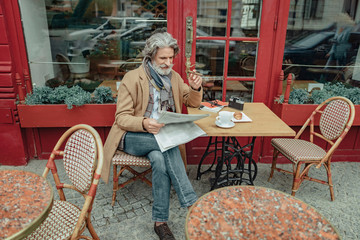 Smiling senior man reading daily news at outdoor cafe