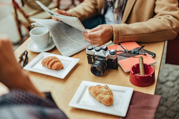 Gentleman sitting at the table with camera, croissants, cigar and cup of coffee
