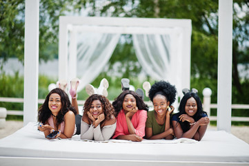 Group of five african american girls relaxing at beautiful poolside cabana beside luxury resort.