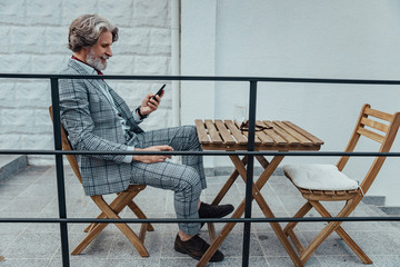 Smiling senior man sitting at the table and using cellphone