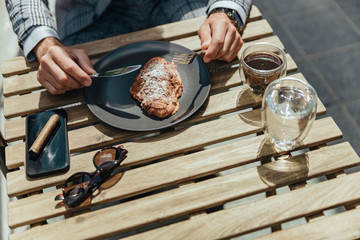 Gentleman with cellphone eating pie at outdoor cafe