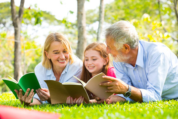 Fototapeta na wymiar Happy Old Grandparents Having Fun With Grandchildren read a book In Park