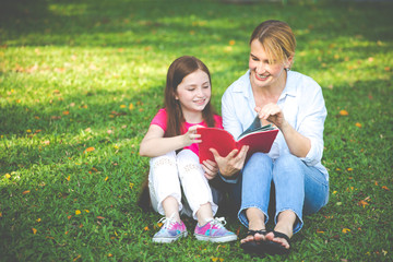 Mother and son are reading a book and smile at the park