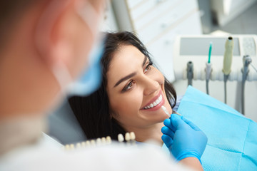 Male stomatologist holding dental crown for smiling woman