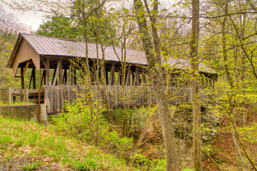 A covered bridge, long abandoned, still stands in the countryside despite being neglected with...