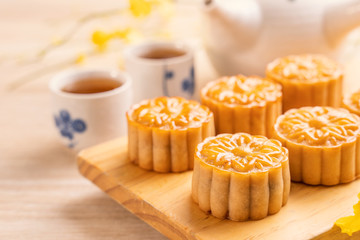 Moon cakes with tea on bright wooden table and serving try, holiday concept of Mid-Autumn festival traditional food layout design, close up, copy space.