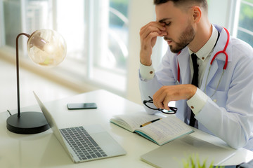 Stressed doctor sitting at his desk in his office while he overworke at the hospital. Medicine, healthcare and people concept.